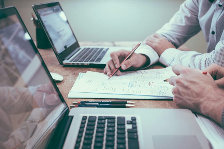 Person holding pencil near laptop on a desk, symbolizing planning and preparation for business financial strategies, in