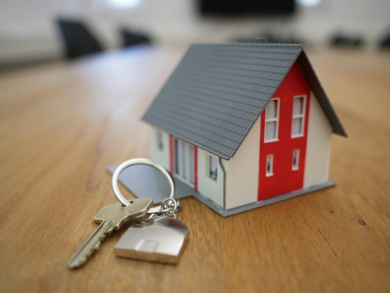 Image: A white and red wooden house miniature on a brown table, representing home ownership and financial planning