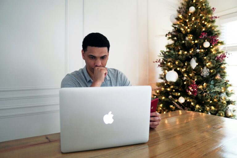 Man in grey crew-neck shirt seated at a desk with a silver MacBook, representing the focused effort